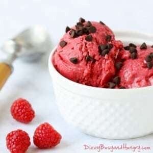 Close up shot of raspberry frozen yogurt sprinkled with chocolate chips in a white bowl with raspberries sprinkled around.