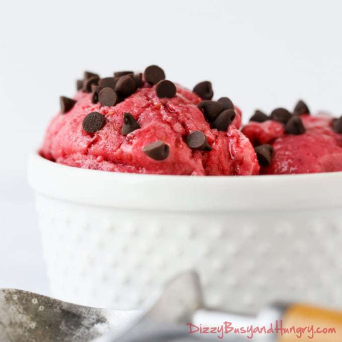 Close up shot of raspberry frozen yogurt sprinkled with chocolate chips in a white bowl.