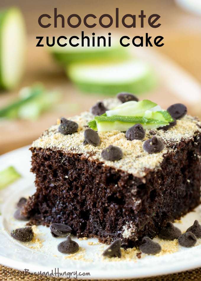 Close up shot of chocolate zucchini cake on a white plate with sliced zucchini in the background. 