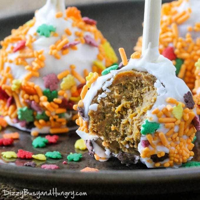 Close up shot of pumpkin cake pops with a bite taken out on a black surface. 