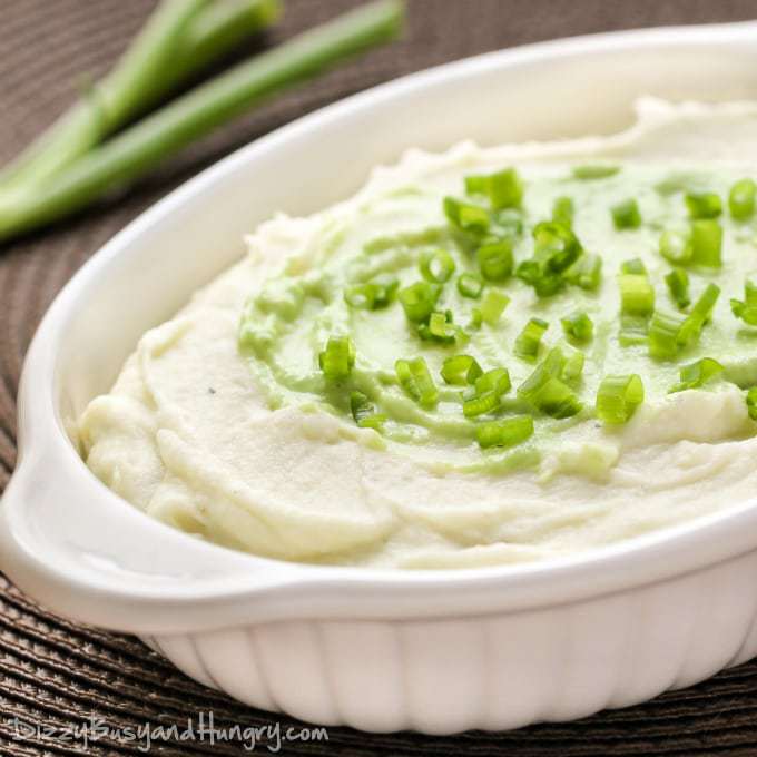 Close up shot of wasabi mashed potatoes sprinkled with chives in a white dish on a brown surface. 