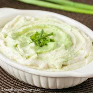 Close up shot of wasabi mashed potatoes sprinkled with herbs in a white dish on a brown surface.