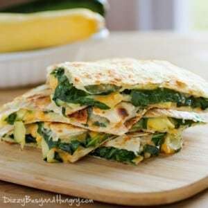 Side shot of cheesy zucchini spinach quesadillas stacked on a wooden cutting board.