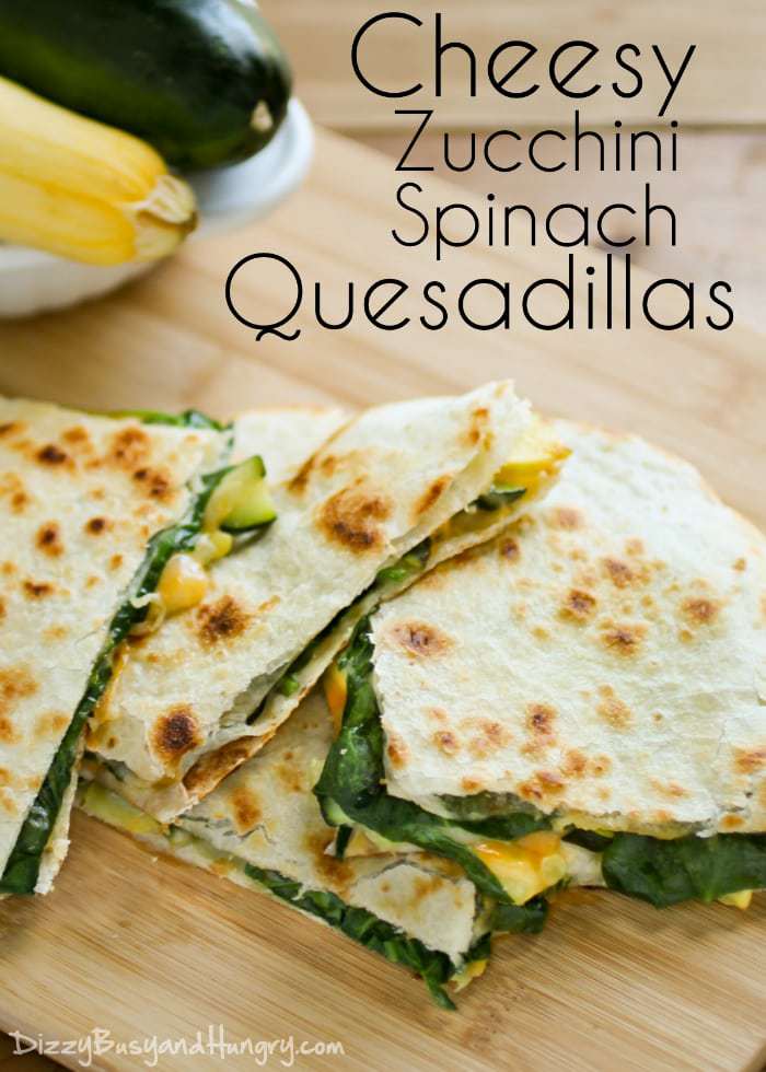 Overhead shot of cheesy zucchini spinach quesadillas layered on a wooden cutting board.