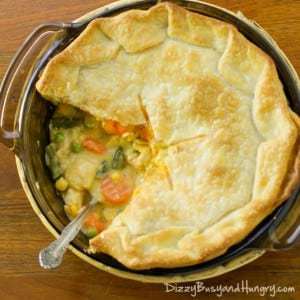 Overhead shot of chicken pot pie in the pan with a slice taken out of it on a wooden surface. 