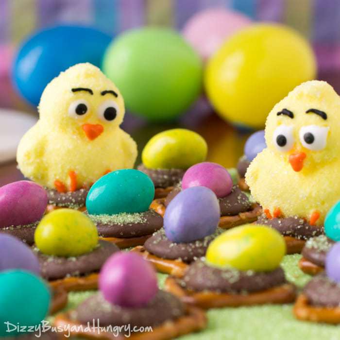 Close up shot of Easter egg peanut butter pretzel bites on a green surface with Easter eggs in the background.