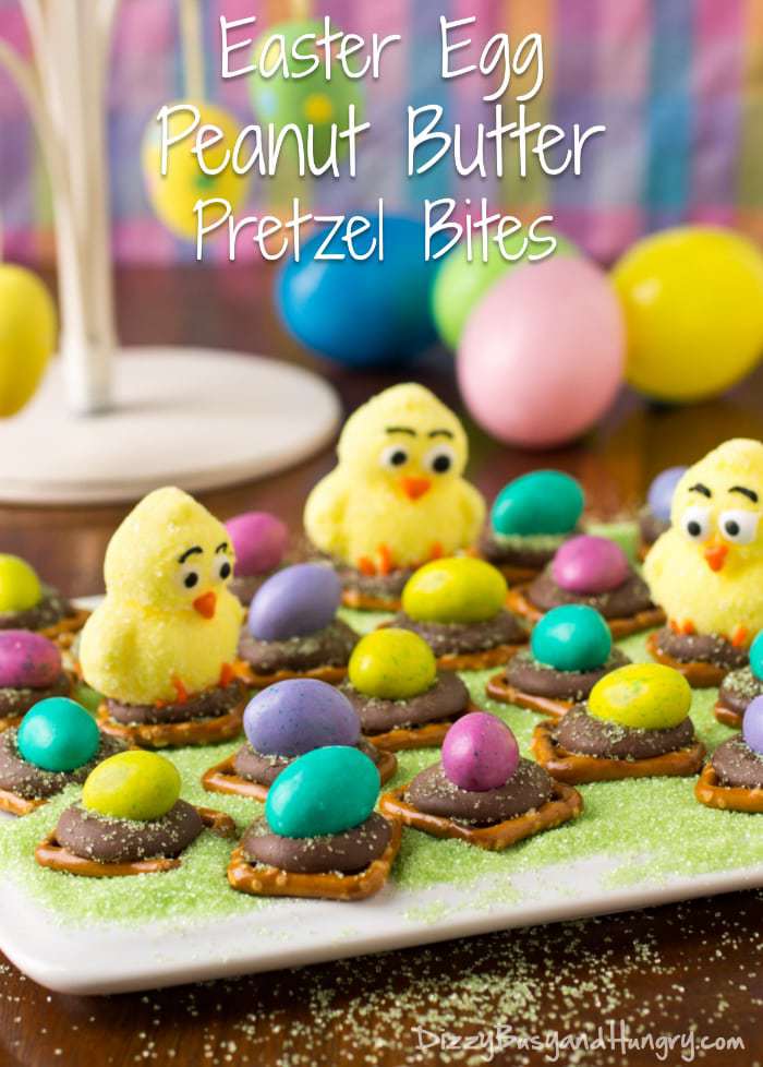 Side view of Easter egg peanut butter pretzel bites on a green surface with Easter eggs in the background. 