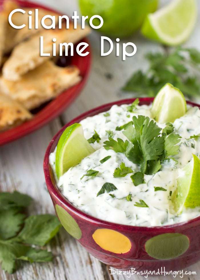 Close up shot of dip garnished with limes and cilantro in a red polka dot bowl with chips and cilantro in the background.