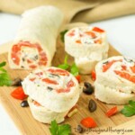 Close up shot of creamy ranch tortilla pinwheels on a wooden cutting board sprinkled with roasted red peppers.