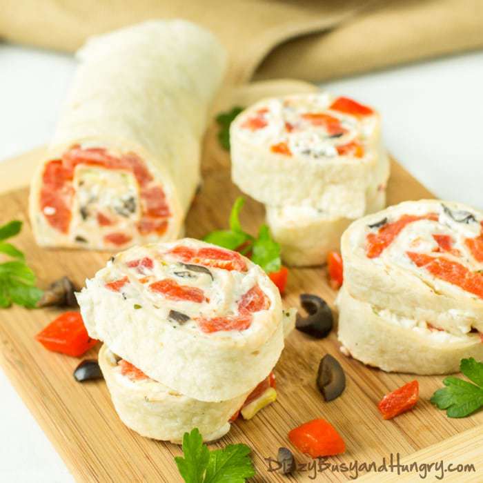 Side shot of creamy ranch tortilla pinwheels on a cutting board sprinkled with sliced olives and red peppers.