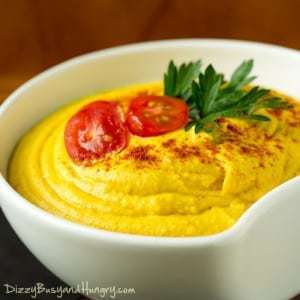 Close up shot of turmeric hummus in a white bowl garnished with tomatoes and herbs.