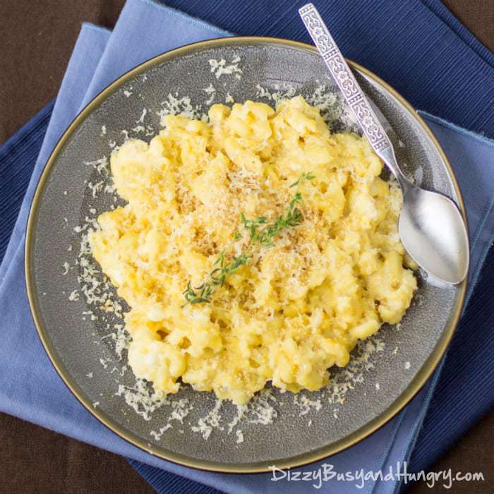 Overhead shot of cauliflower Mac and cheese garnished with herbs on a grey plate with a spoon on the side on a blue cloth. 