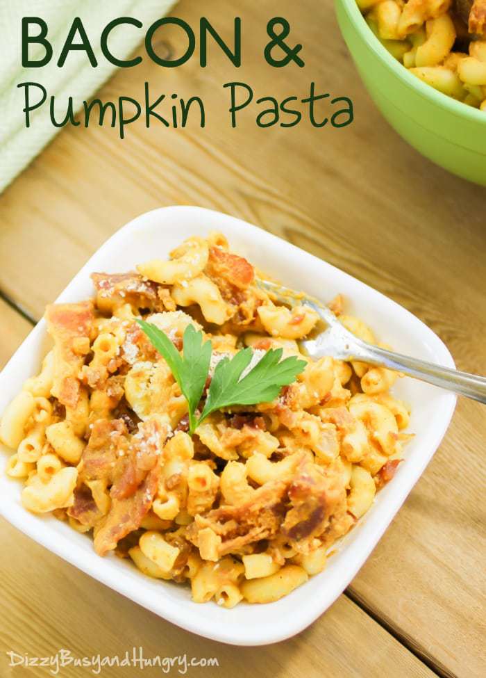 Side view of bacon and pumpkin pasta garnished with herbs in a white bowl with a fork on the side on a wooden surface