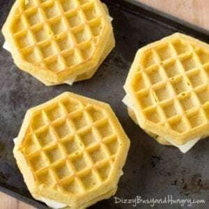 Overhead shot of three waffle breakfast sandwiches on a metal pan.