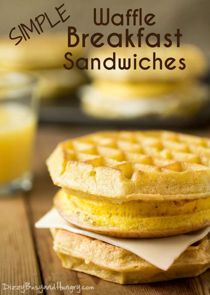 Side view of a waffle breakfast sandwich on a wooden surface with more in the background on a metal pan. 