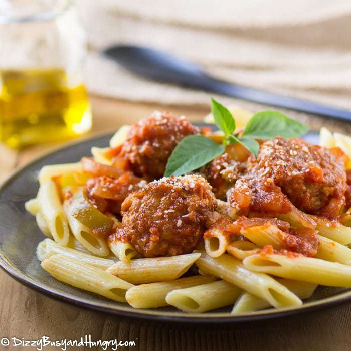 Side view of chicken cacciatore meatballs on penne pasta garnished with herbs on a black plate. 