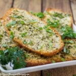 Side shot of Parmesan Garlic bread layered on a white plate on a wooden surface.