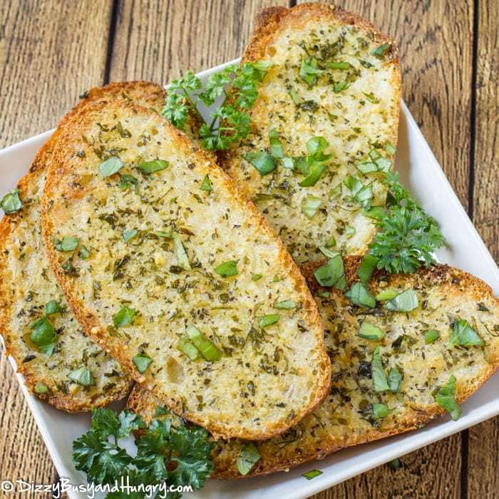 Overhead shot of Parmesan Garlic bread layered on a white plate on a wooden surface. 