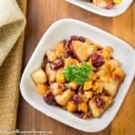 Overhead shot of two white bowls of butternut squash and apples on a wooden surface with a tan cloth on the side.