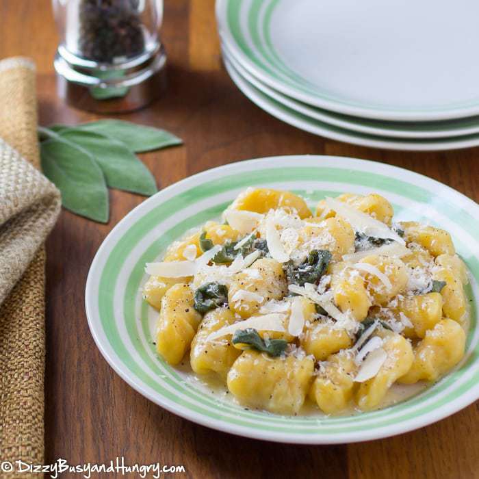 Close up shot fo squash gnocchi sprinkled with shredded parmesan on a green and white striped plate.