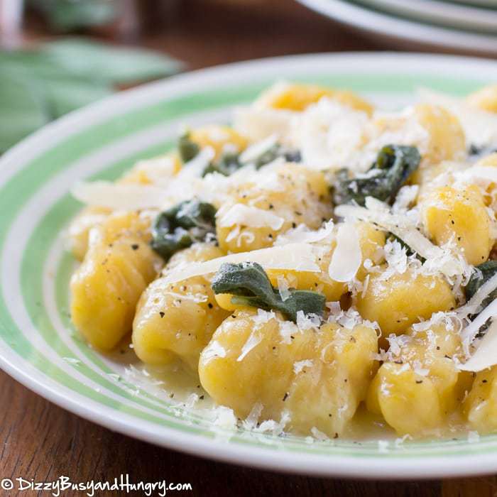 Close up shot fo squash gnocchi sprinkled with shredded parmesan on a green and white striped plate.