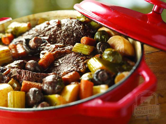 Close up shot of braised pot roast with root vegetables in a red pot. 
