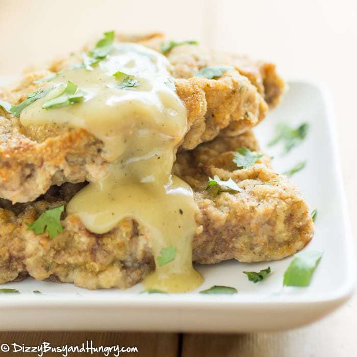 Up close view of two pieces of chicken fried steak on a white plate with a yellow gravy