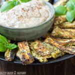 Side shot of eggplant fries surrounding a bowl of basil dipping sauce garnished with herbs.