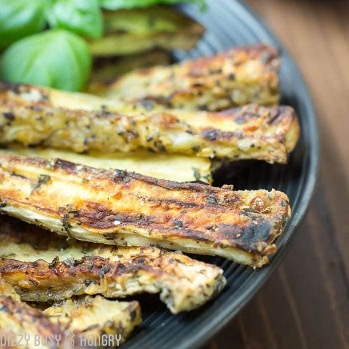 Close up shot of eggplant fries garnished with herbs on a black plate. 