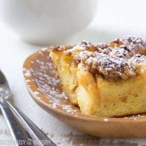 Close up shot of butterscotch French toast bake on a wooden plate sprinkled with powdered sugar with silverware on the side.