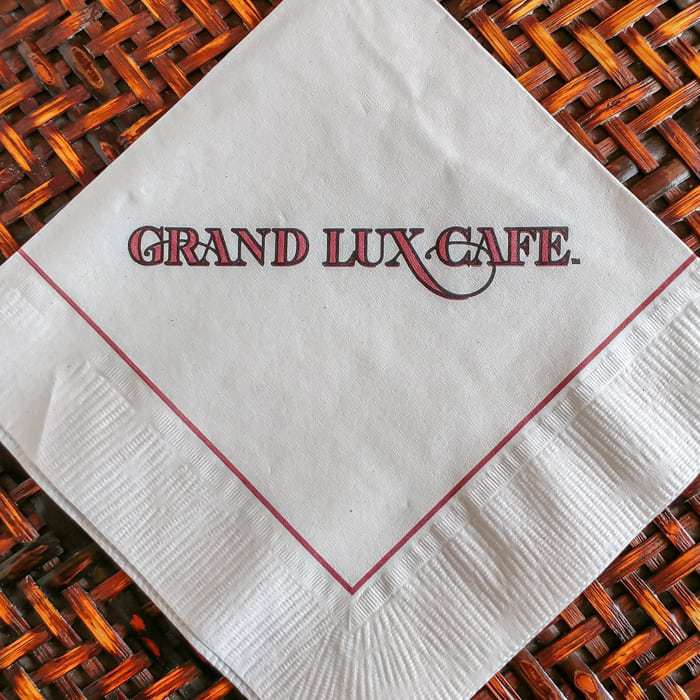 Close up of a paper napkin with the words \"Grand Lux Cafe\" written. 
