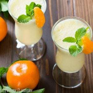 Overhead shot of pineapple orange smoothie in two wine glasses garnished with orange and mint.