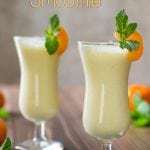 Side shot of pineapple orange smoothie in two wine glasses garnished with orange and mint. 