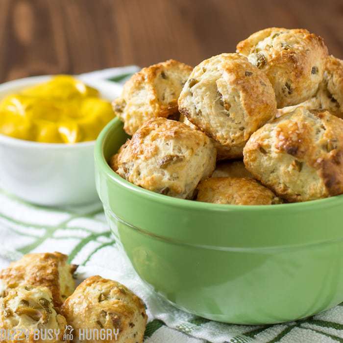 Side shot of olive parmesan pretzel bites in a green bowl on a white and green striped cloth. 