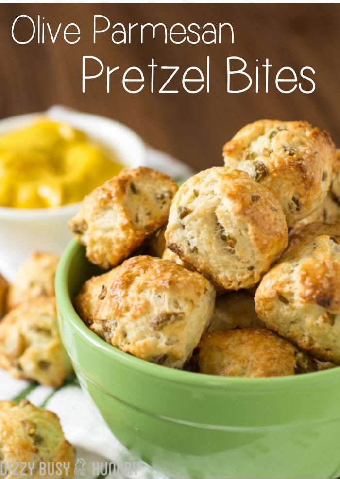 Side view of olive parmesan pretzel bites stacked in a green bowl with lemons in the background. 