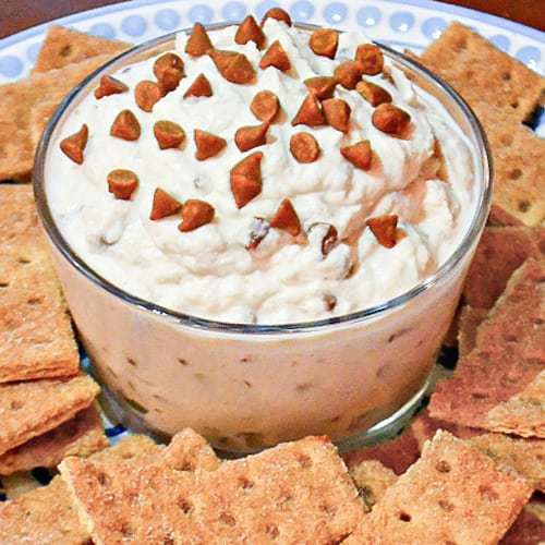 Close up shot of cinnamon cannoli dip in a clear bowl surrounded by graham crackers on a blue plate.