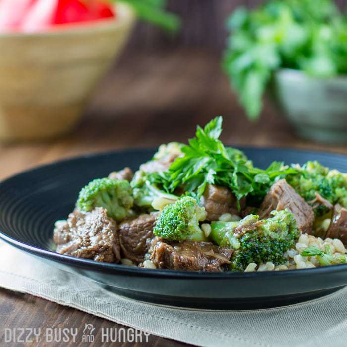 Facet behold of crock pot crimson meat and broccoli on a dim plate on a white cloth with peppers and herbs within the background.  Crock Pot Beef and Broccoli crock pot recipes beef and broccoli 3