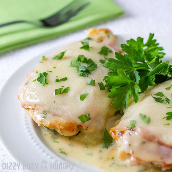 Two pieces of chicken Cordon Bleu sprinkled with herbs on a white plate with a green cloth and fork on the side. 