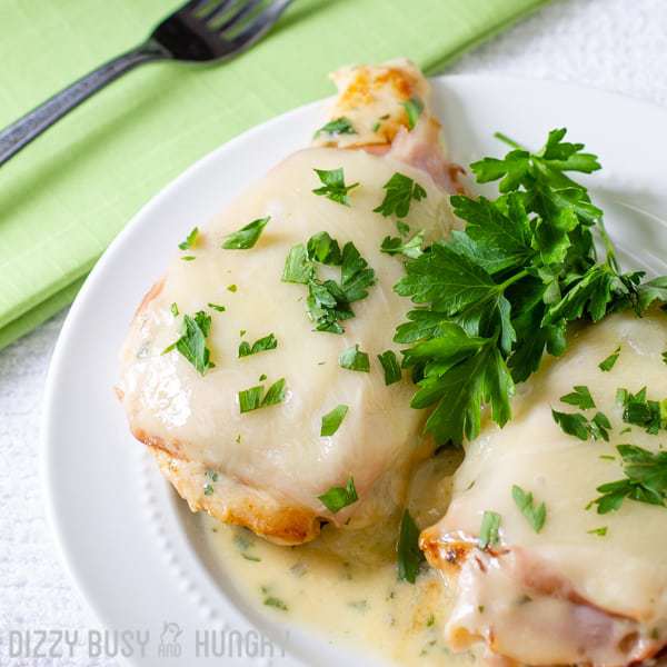Close up shot of two pieces of chicken Cordon Bleu sprinkled with herbs on a white plate with a green cloth and fork on the side. 