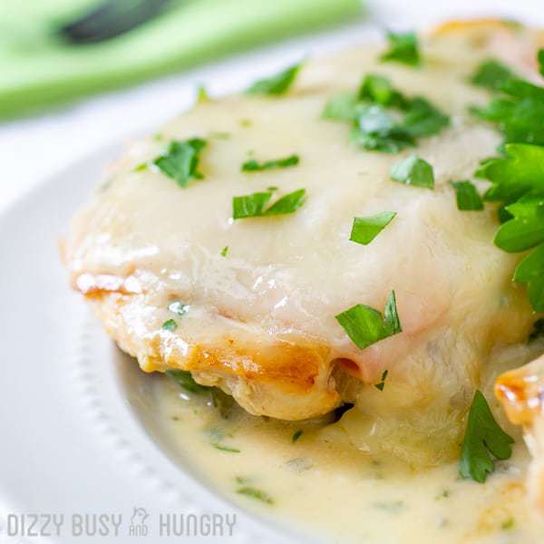 Close up shot of Chicken Cordon Bleu sprinkled with herbs on a white plate with a green cloth and fork on the side. 