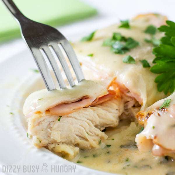 Close up shot of a fork taking a piece of the Chicken Cordon Bleu sprinkled with herbs on a white plate.