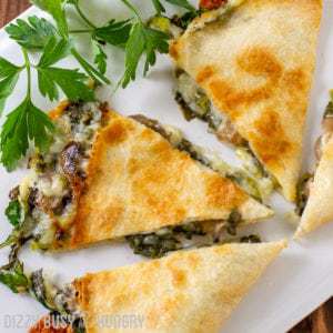 Overhead shot of baked spinach mushroom quesadillas sliced into pieces on a white plate with herbs on the side.