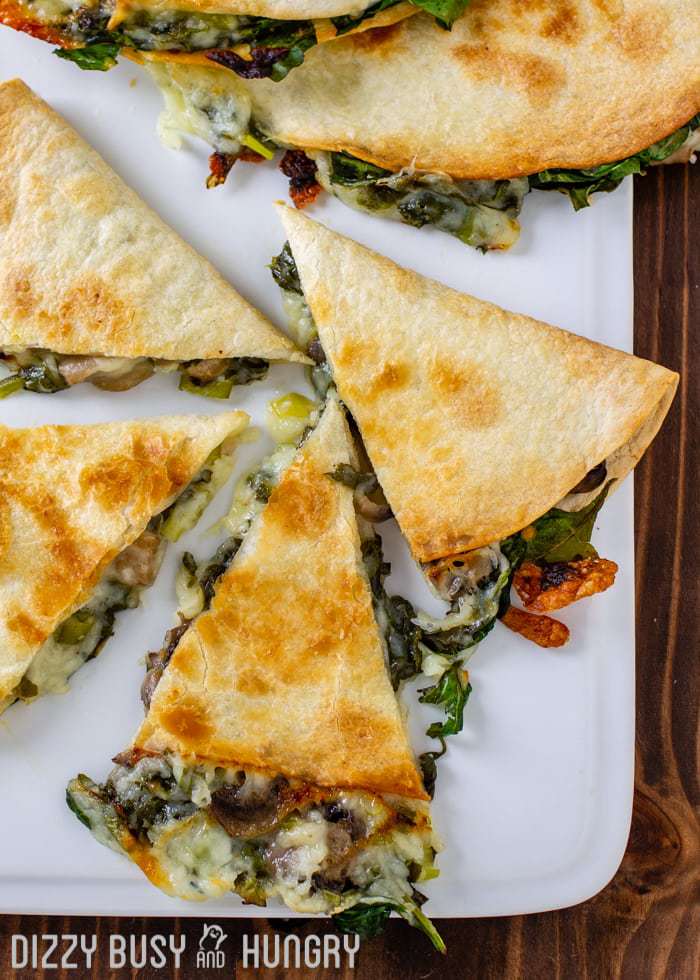 Overhead shot of baked spinach mushroom quesadillas sliced into pieces on a white plate.