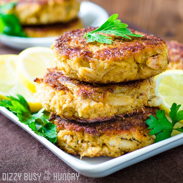Side view of three stacked crab cakes grilled golden brown and garnished with lemon slices and parsley.