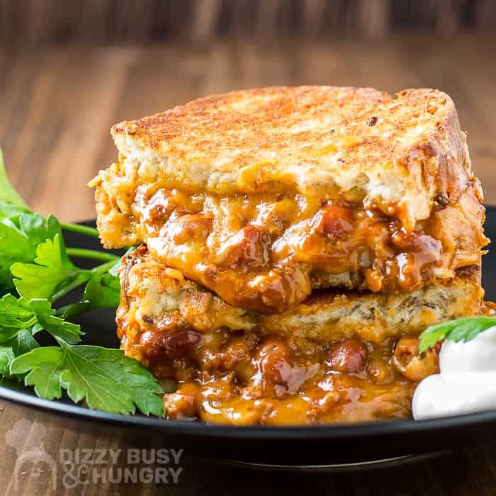 Side view of chili cheese grilled sandwich cut in half with herbs and sour cream on a black plate.