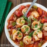 Overhead shot of shrimp stew sprinkled with herbs in a white bowl with a green cloth on the side.