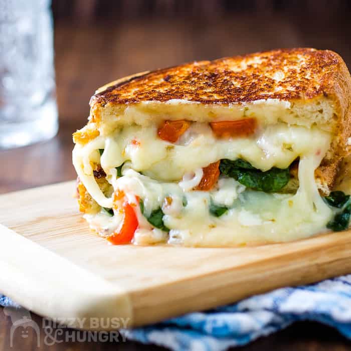 melty grilled cheese with roasted red peppers and spinach stacked on a cutting board