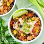 Overhead shot of crock pot enchilada bake in a white bowl with a lime  and herbs on the side.