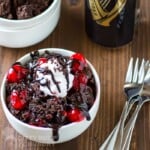 Side view of Guinness chocolate cake in a white bowl with forks and a glass in the background.