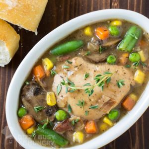 Overhead shot of crock pot Guinness chicken stew in a white oval bowl with sliced bread on the side.